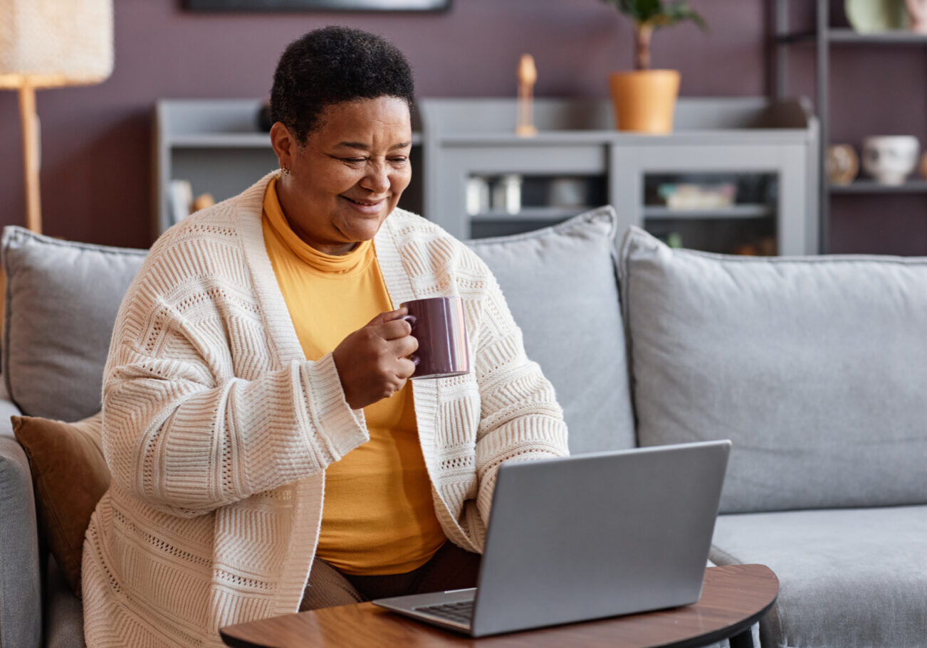 Portrait of senior black woman using laptop at home and enjoying cup of coffee, copy space