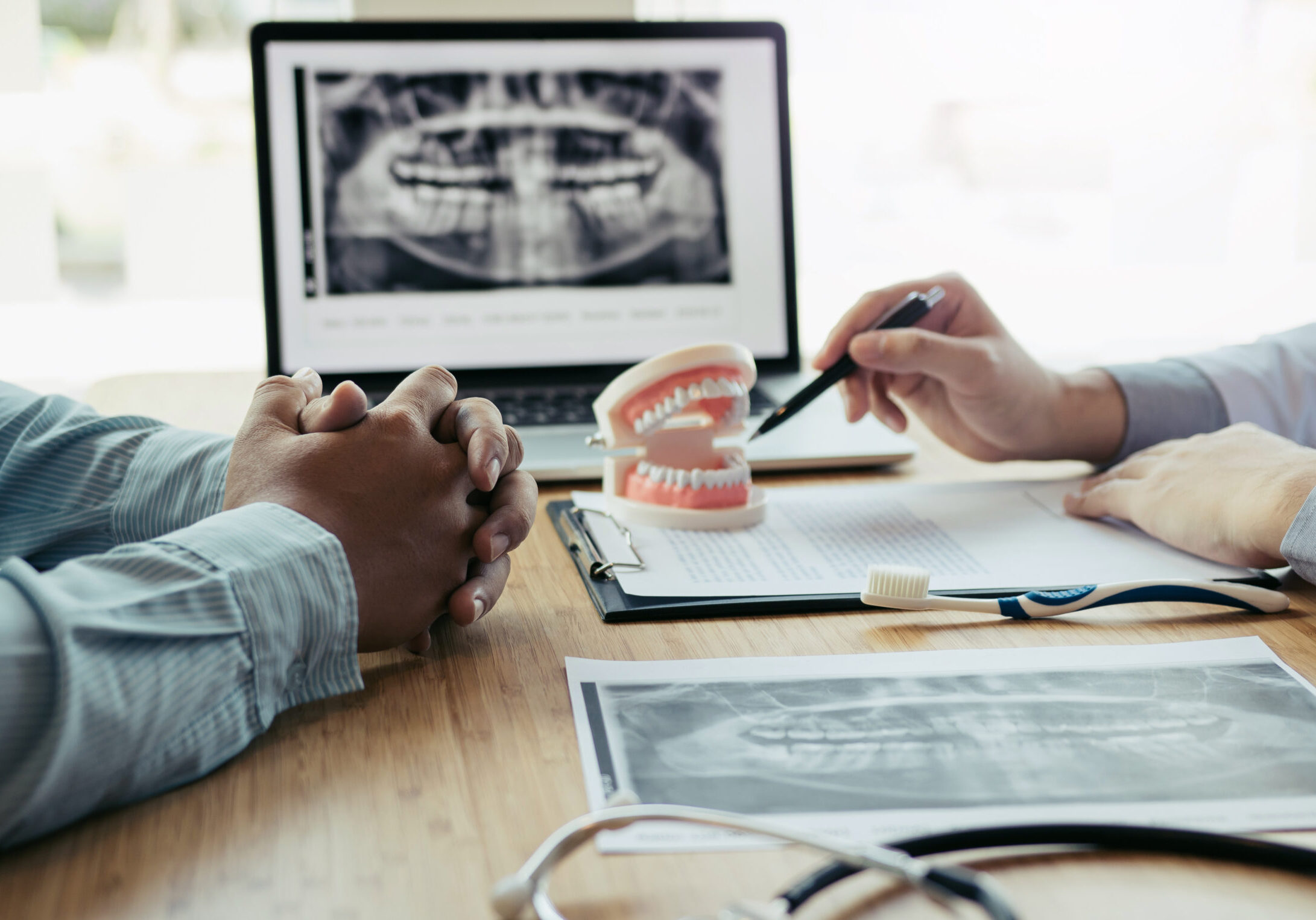 Dentists are discussing dental problems at report x-ray image on laptop screen to patients.
